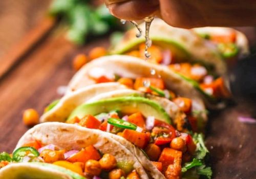 A hand squeezing lime juice over a row of fresh vegetable tacos on a wooden surface, with vibrant ingredients like chickpeas, red onions, and avocado.