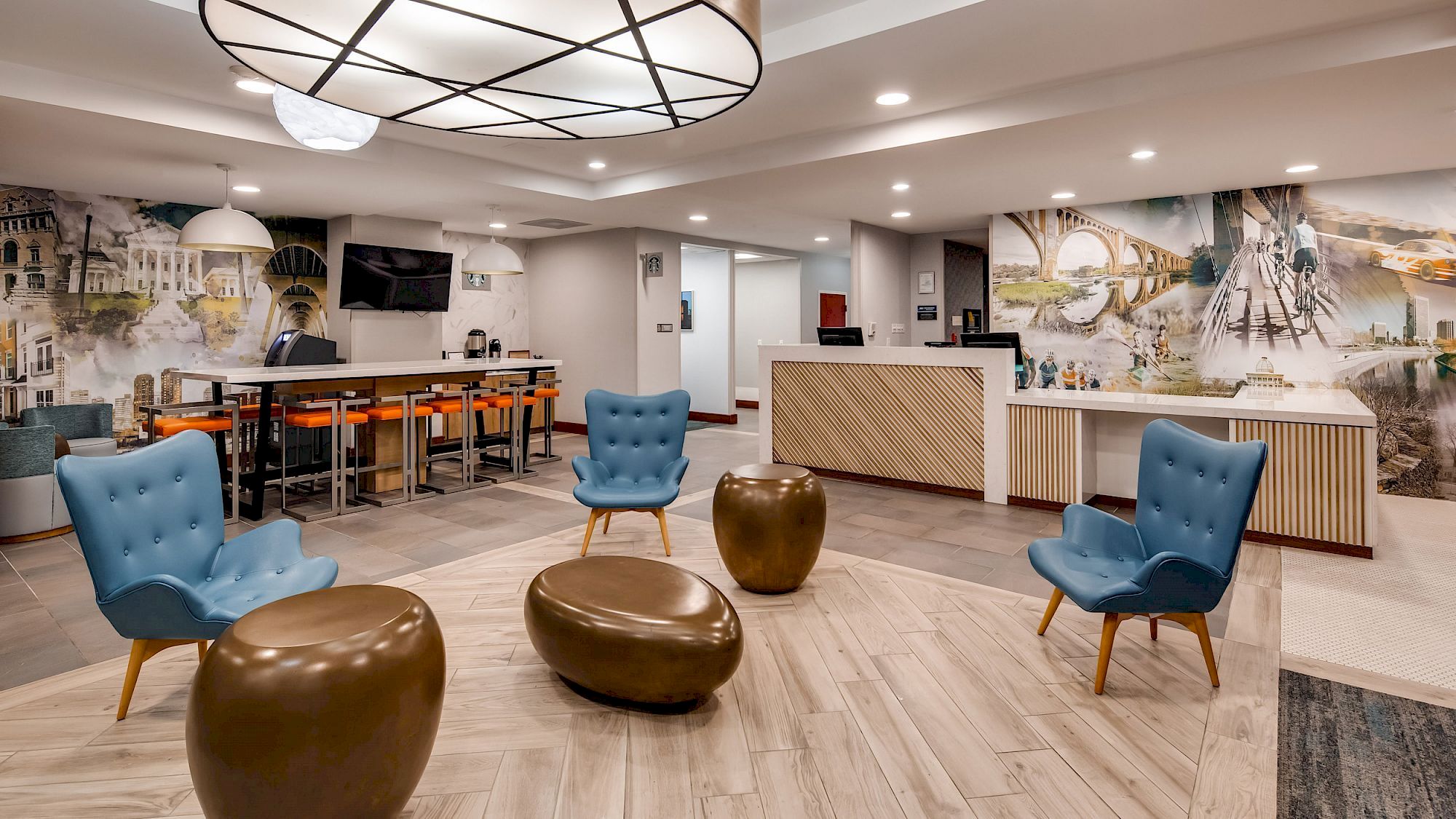 A modern lobby with blue chairs, brown ottomans, a front desk, wall art, bar seating, and contemporary lighting fixtures ends the sentence.