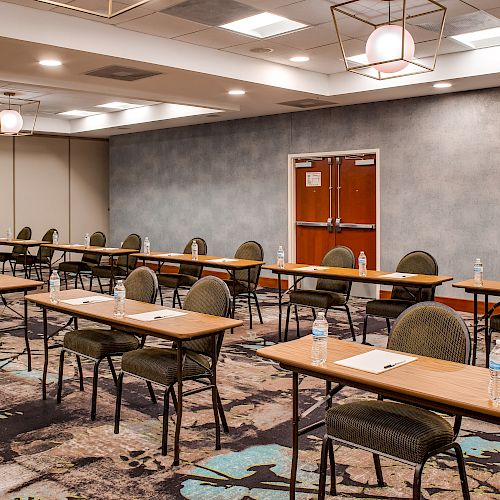 The image shows an empty conference room with several rows of tables and chairs arranged facing the front.