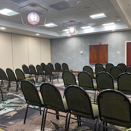 An empty conference room with multiple rows of green chairs and modern pendant lighting is shown.