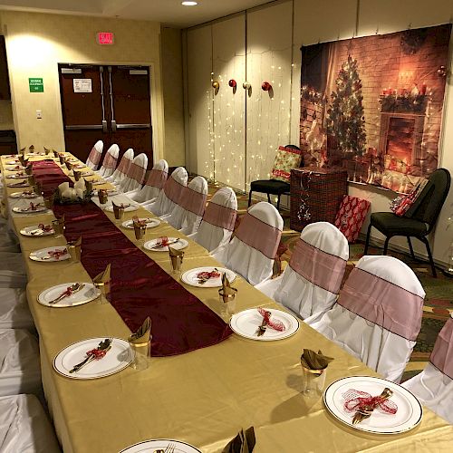 A dining room set for a holiday gathering, featuring a decorated long table with plates, napkins, and chairs, and festive decor on the wall.