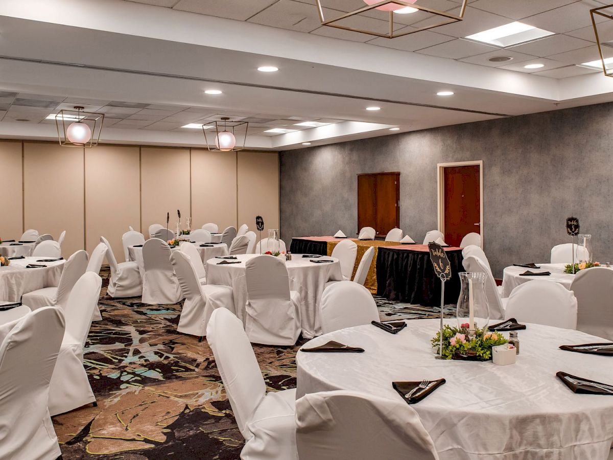 The image shows a decorated banquet hall with round tables covered with white tablecloths and chairs, set up for an event or function.
