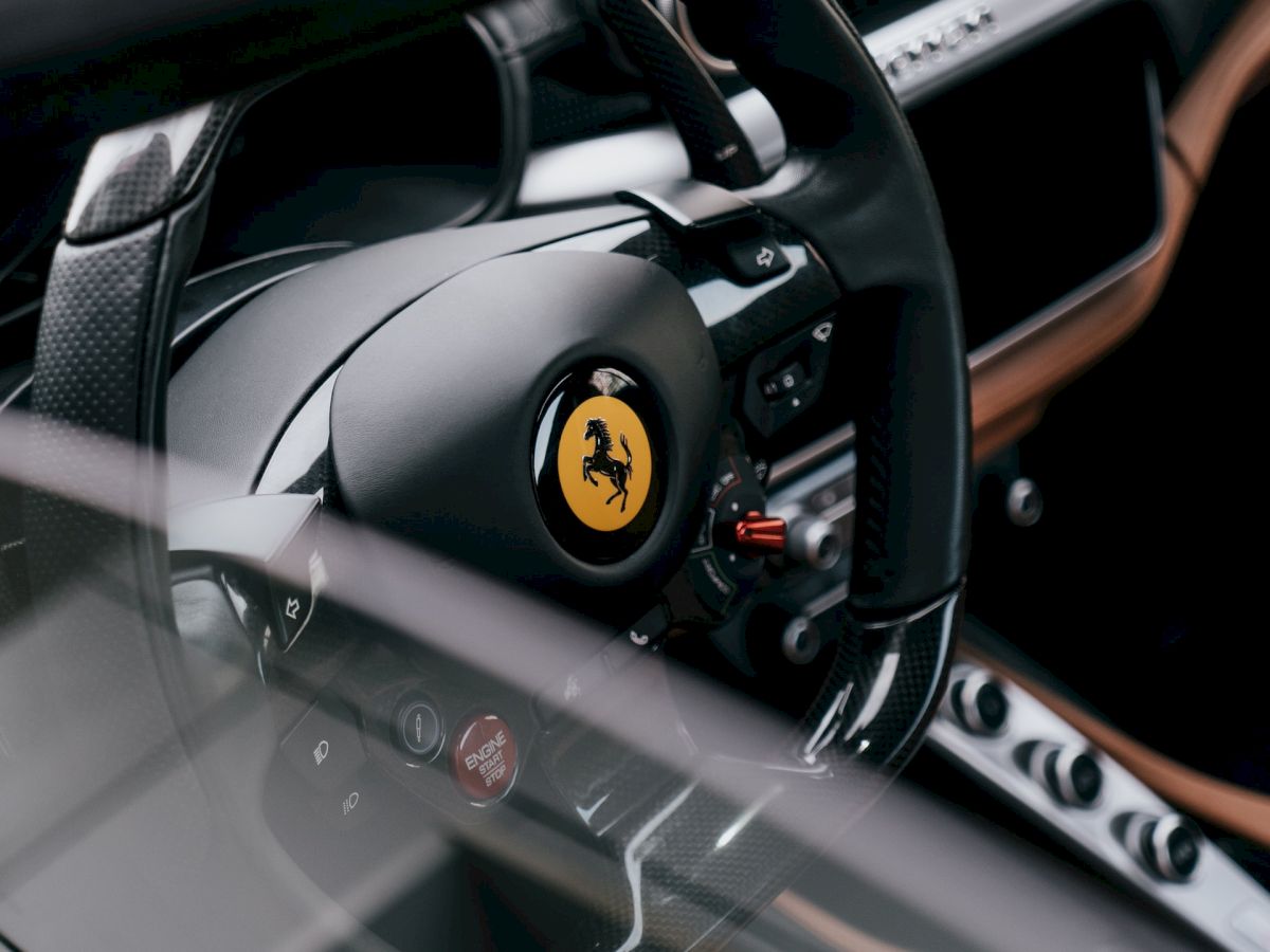 The image shows the interior of a Ferrari sports car, with a focus on the steering wheel featuring the iconic yellow prancing horse logo.