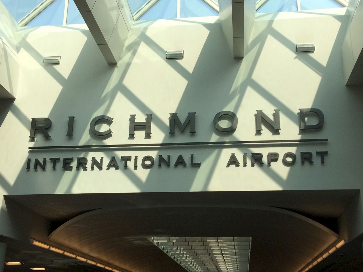 The image shows a sign for Richmond International Airport, with sunlight casting shadows through a skylight above.