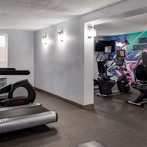A gym with treadmills, ellipticals, and a motivational mural saying 