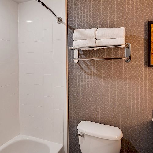 A bathroom with a white bathtub, towel rack with folded towels, a toilet, a countertop with a sink, and a framed picture on the wall ending the sentence.
